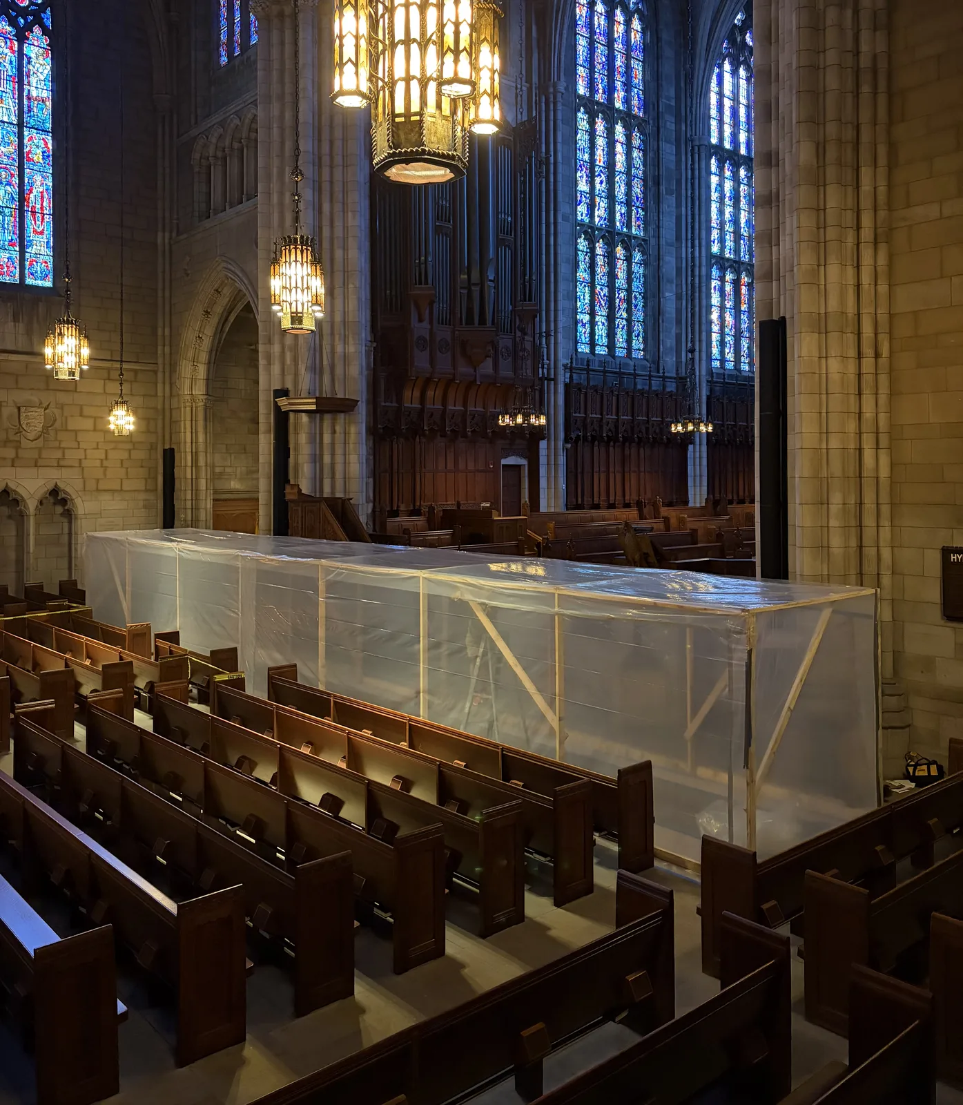 Protective enclosure built over the work area inside the Princeton University Chapel, with stained glass and pendant lanterns beyond.